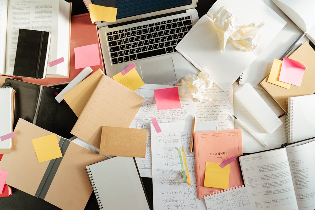 Overwhelmed workspace covered in notebooks, sticky notes, crumpled papers, and an open laptop—representing the chaos of disorganized finances and the need for professional QuickBooks Online cleanup services for small businesses.